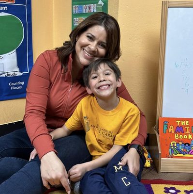 Alejandra Soria, Lead Teacher at Kirsis' Daycare, smiling with a child in the classroom