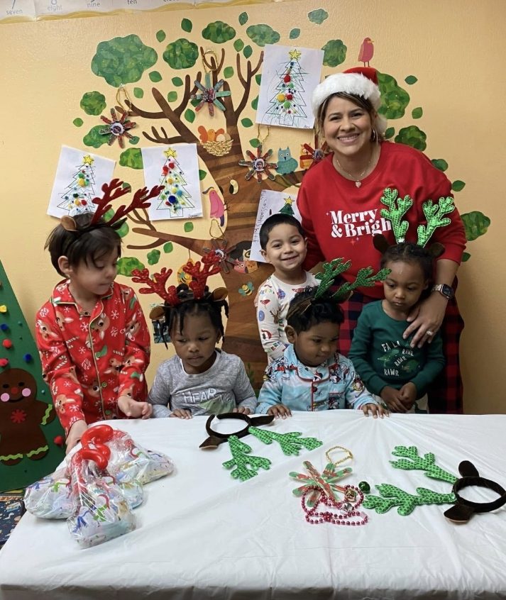 Teacher and children in holiday pajamas and reindeer antler headbands posing for a Christmas party photo
