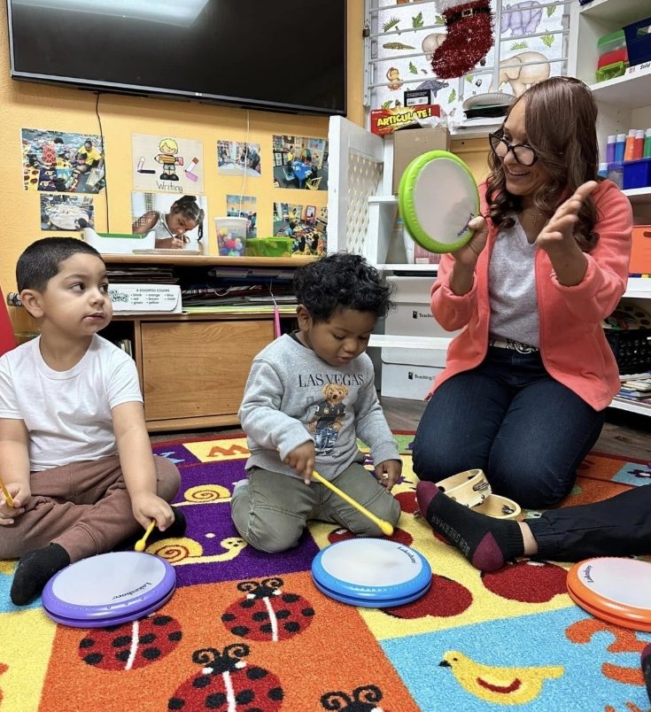 Teacher playing hand drums with two children during a music activity in the classroom