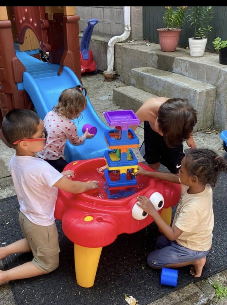 Four children playing together at an outdoor water play table next to a slide